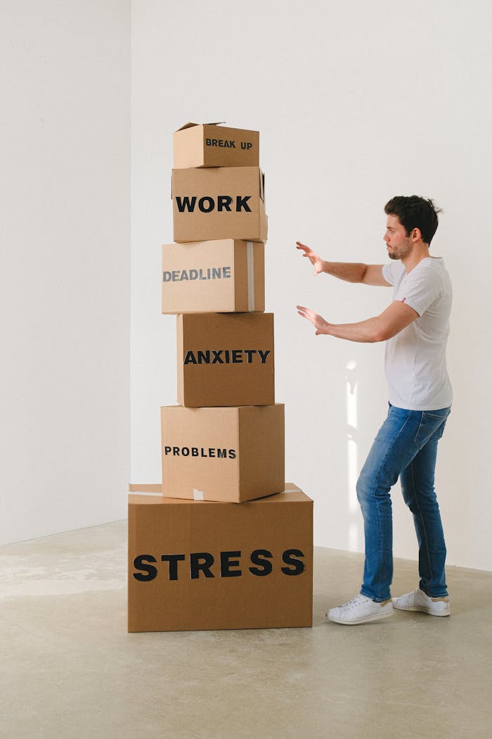 A man in casual attire balances boxes labeled with stress-related words indoors.